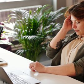A businesswoman feeling stressed at her home office desk while working on her laptop.