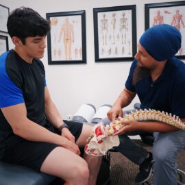 A doctor explains spinal issues to a patient using a spine model during a medical consultation, chiropractor mandurah